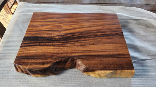 Finished live edge wood slab with dark streaked grain, a pale sapwood band and a natural curved edge, resting on protective foam in the Woodfurnist workshop in Da Nang