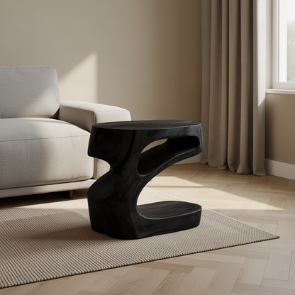 Zephyra sculptural wood side table in Black with twisting open form beside a modern armchair