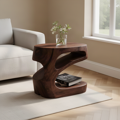 Zephyra sculptural wood side table in rich Brown finish with books on its open shelf beside an armchair