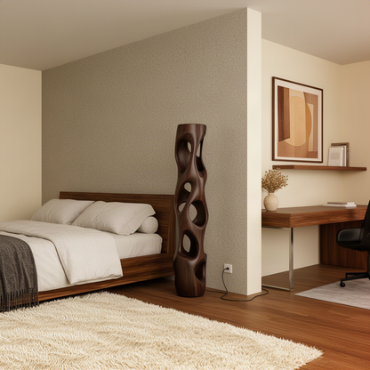 Ambera hollow wood column lamp in a dark finish standing beside the bed as a sculptural accent in a calm bedroom