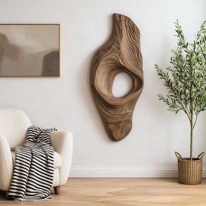 Driftara organic wood wall art hung between an armchair and an olive tree in a calm neutral living room